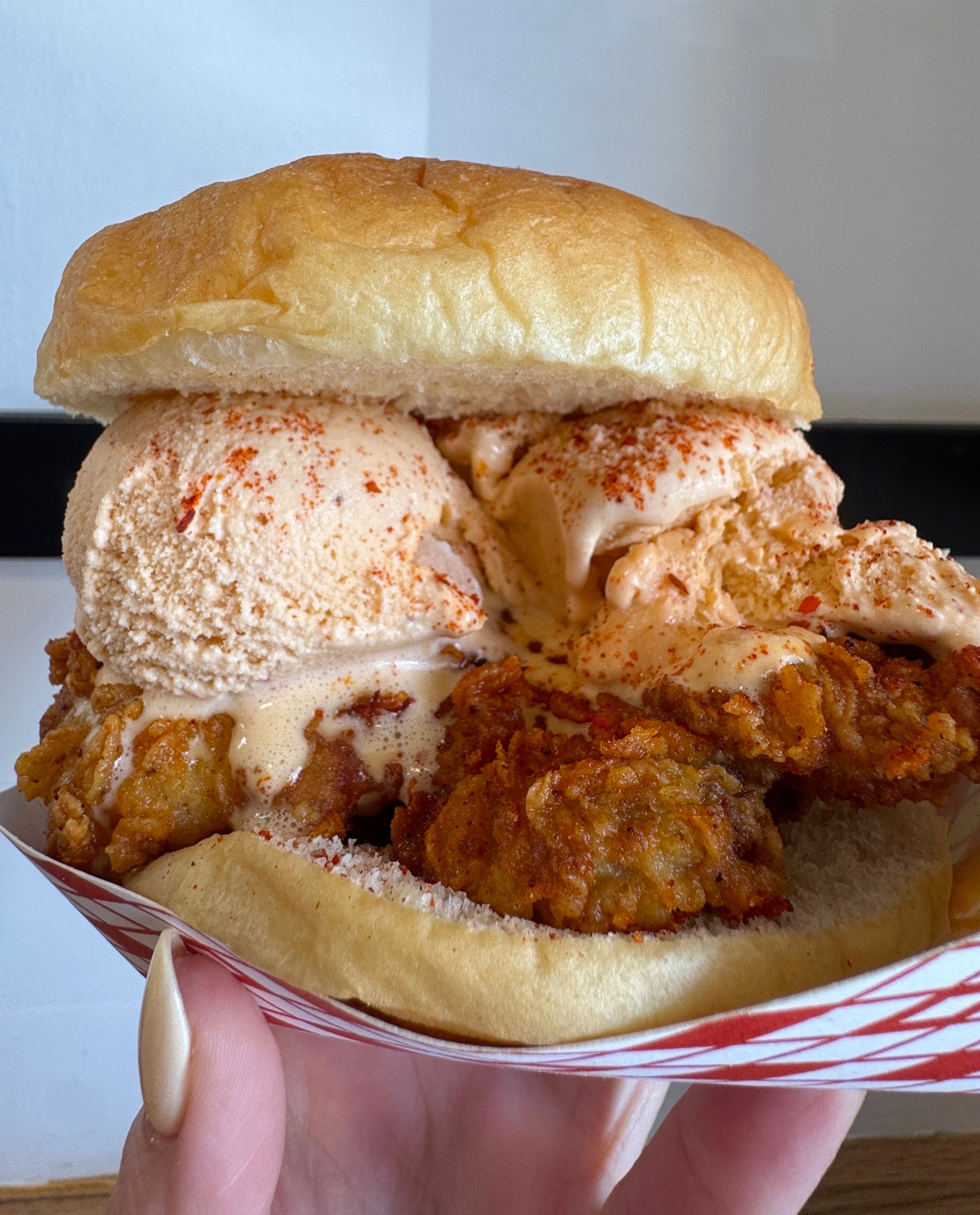 A sandwich with fried chicken and ice cream scoops being held up by a hand.
