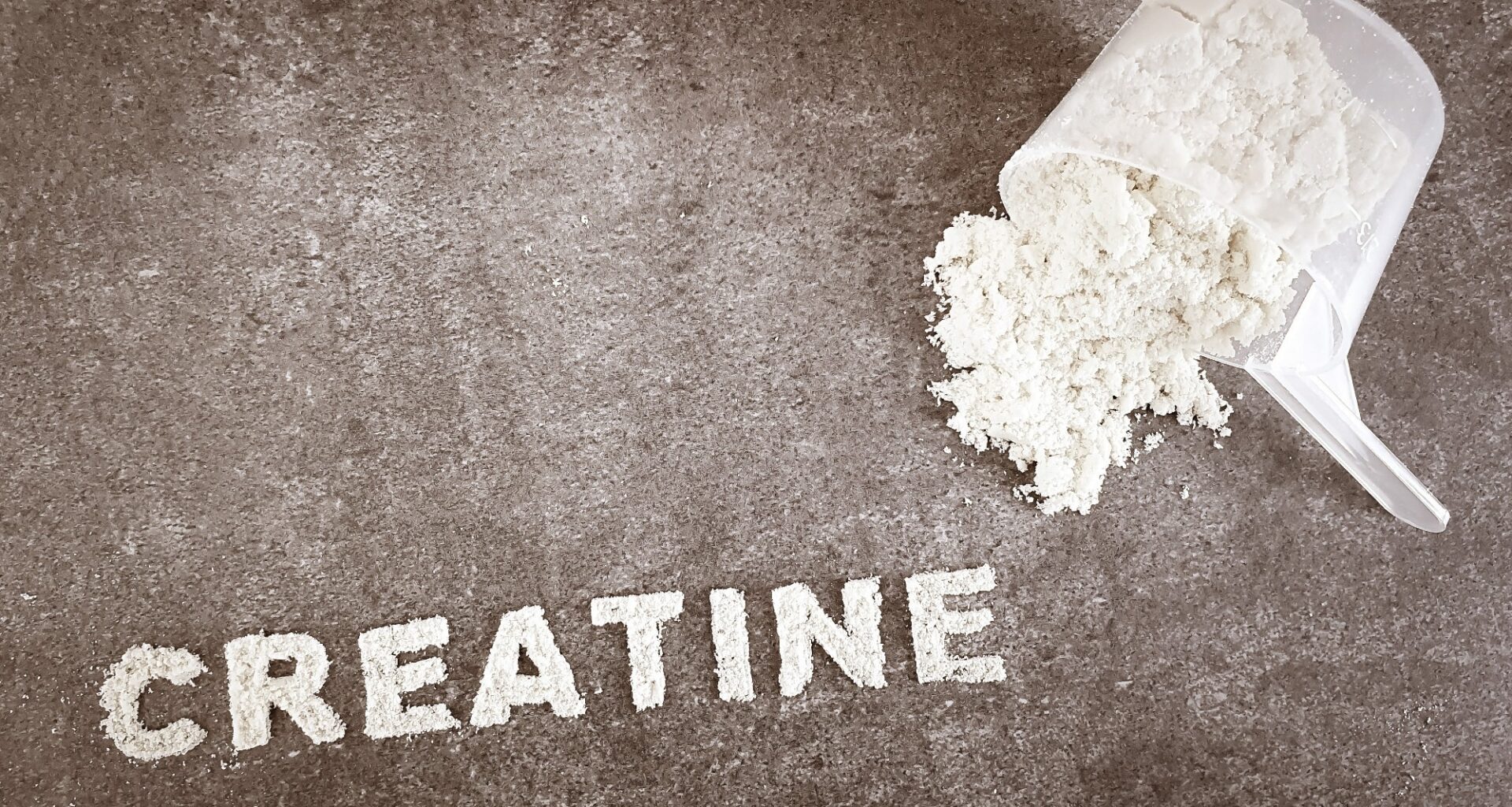 Creatine powder text font on grey stone background with plastic spoon cup