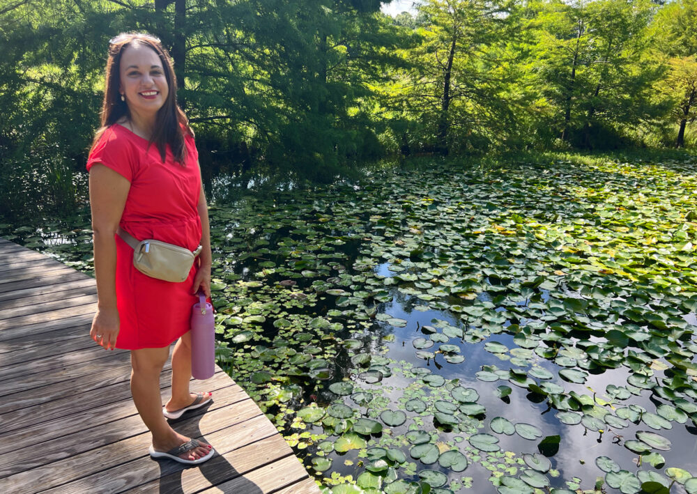 A woman in a red dress stands next to a pond
