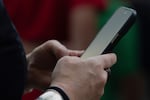 FILE - The scams start innocuously, often with a tailor-made text or WhatsApp message, and the scammers take time to build trust with the victim before cashing in on the relationship. A person looks at their phone at Seattle–Tacoma International Airport in this Sunday, June 1, 2025 file photo.