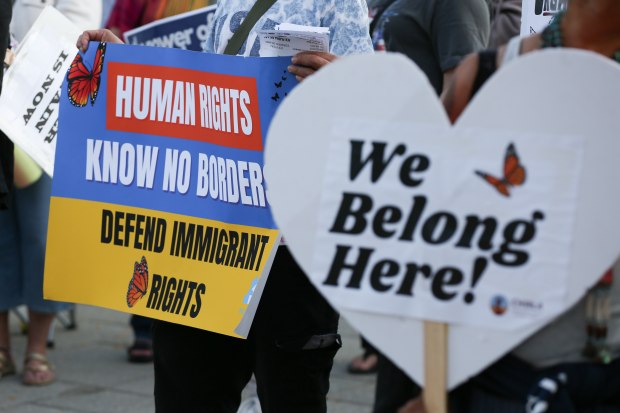 Protesters hold signs as they listen to speakers during a...