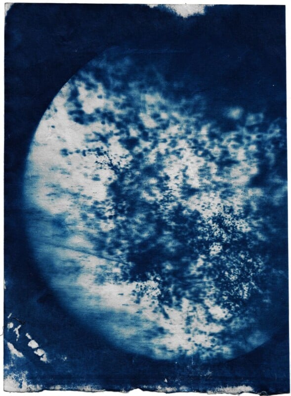 Abstract blue and white image resembling a circular shape with cloudy or speckled patterns, appearing like a textured watercolor or a stylized view of a planet or the moon.