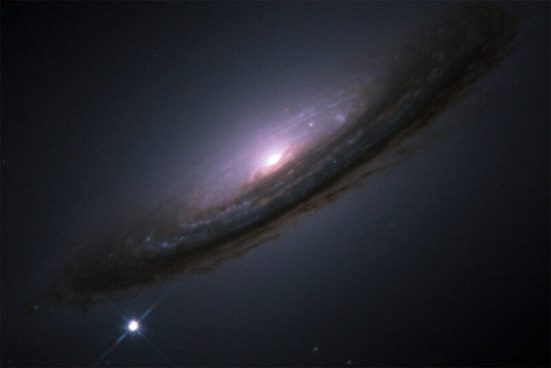 An oblique view of a spiral galaxy with a bright star next to it.