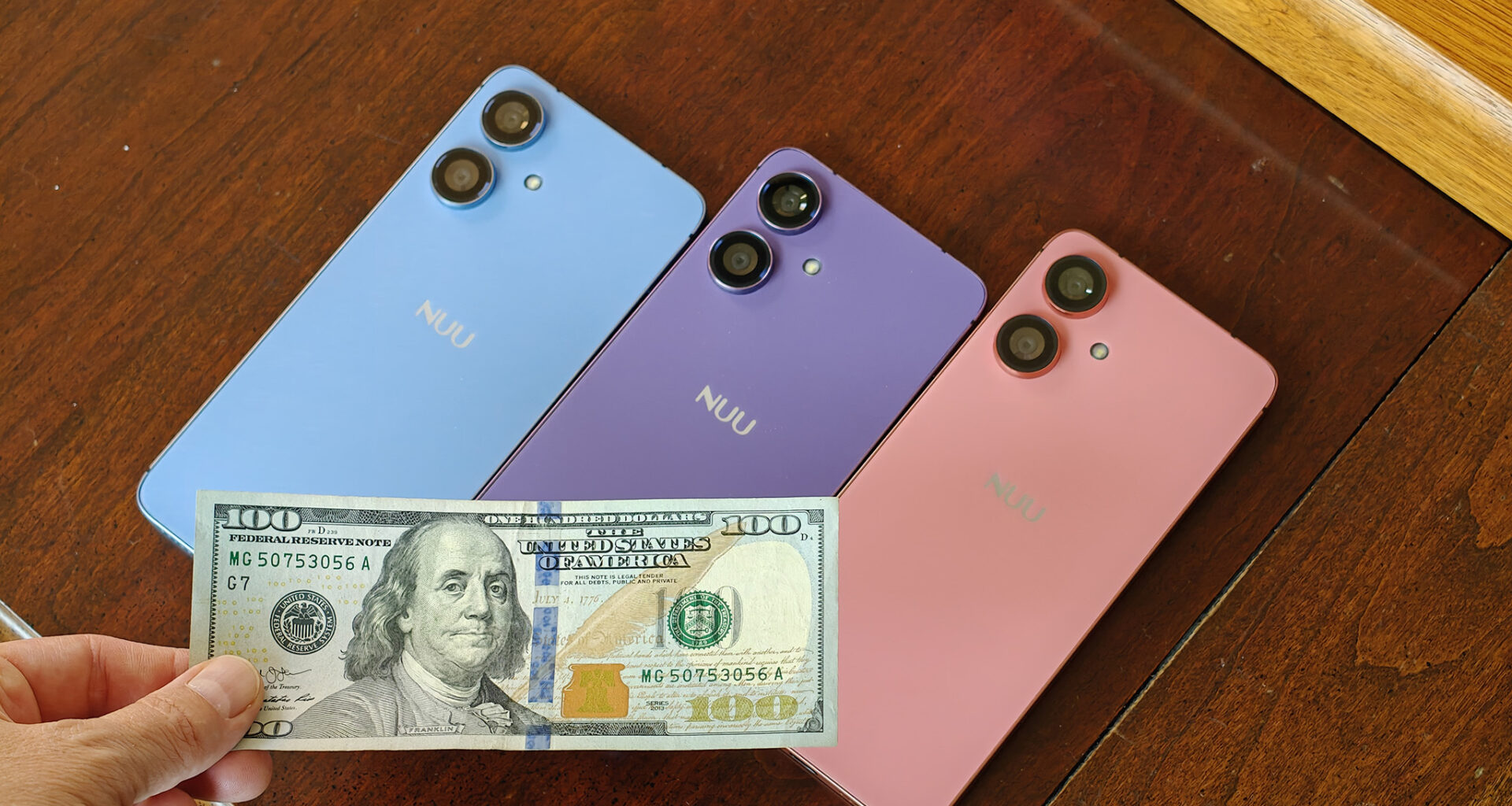 Three different Nuu N20 phones in blue, purple, and pink, with a $100 bill on front of them