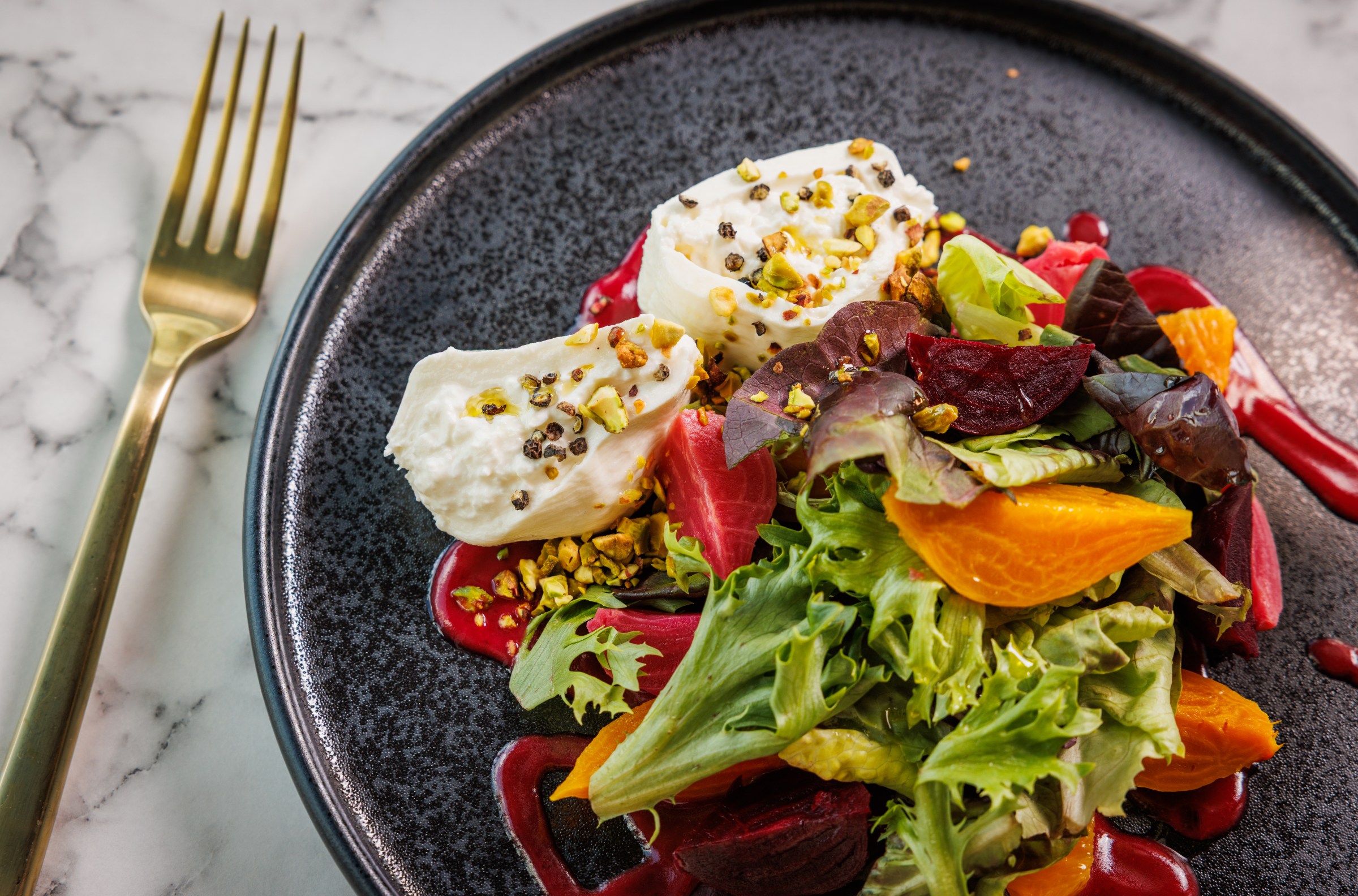 A roasted beet salad with burrata sits on a black plate.