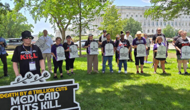 A group of protesters stand holding signs. One large sign reads, "Death by a trillion cuts: Medicaid cuts kill." Others hold signs shaped like tombstones that read, "Here lies America's future," and "R.I.P. Sacrificed for the rich."
