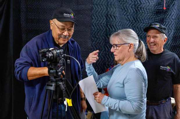In the garage of Kevin and Heather Marty, Pace-TV San Diego President Ernie Alvarez, left, speaks to camera operator Leslie Couch as the video team prepares to shoot an episode of the show. This one will be an interview with Glenn Wise, of Mesa View Baptist Church in Poway, about the church's food bank. At far right is the show's Director Kevin Marty. (Charlie Neuman / For The San Diego Union-Tribune)