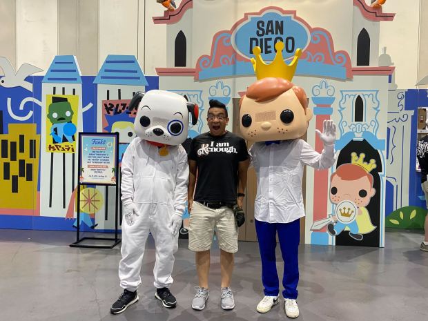 Funko fan Ken Leung is greeted by Freddy and Proto at the Funko booth inside the exhibit hall. (David J. Bohnet / The San Diego Union-Tribune)
