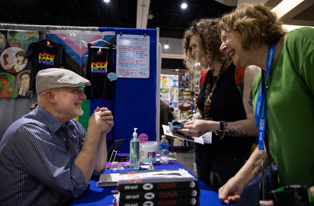 Jon Macy, left, signs autographs and speaks to Sonya Saturday, center, and Millie Tanner while selling one of his graphic novels during the San Diego Comic-Con at the Prism Comics table on Thursday, July 24, 2025 in San Diego, California. (Ana Ramirez / The San Diego Union-Tribune)