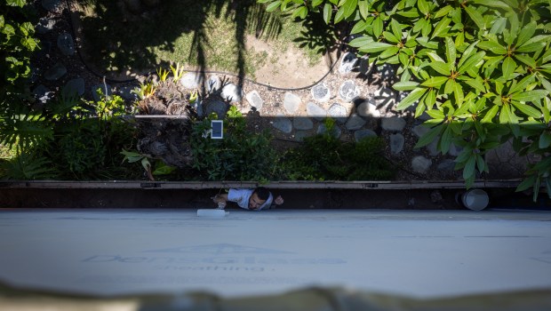 A worker squeezes between a fence and a wall to finish painting an ADU on Tuesday, July 29, 2025 in San Diego. (Ana Ramirez / The San Diego Union-Tribune)