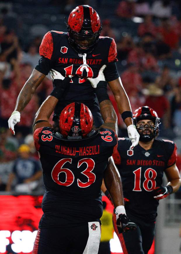 San Diego State offensive lineman Ross Ulugalu-Maseuli (63) lifts wide receiver Jordan Napier (19) after a touchdown against Texas A&M-Commerce during their game at Snapdragon Stadium on Saturday, Aug. 31, 2024 in San Diego, CA. (Meg McLaughlin / The San Diego Union-Tribune)