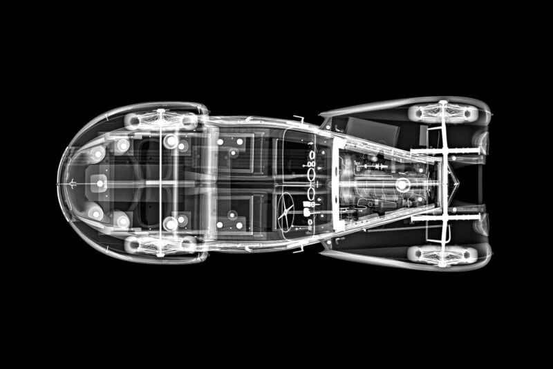 X-ray view of a classic car from above, showing the car’s internal structure, seats, steering wheel, and mechanical components, all outlined in white against a solid black background.