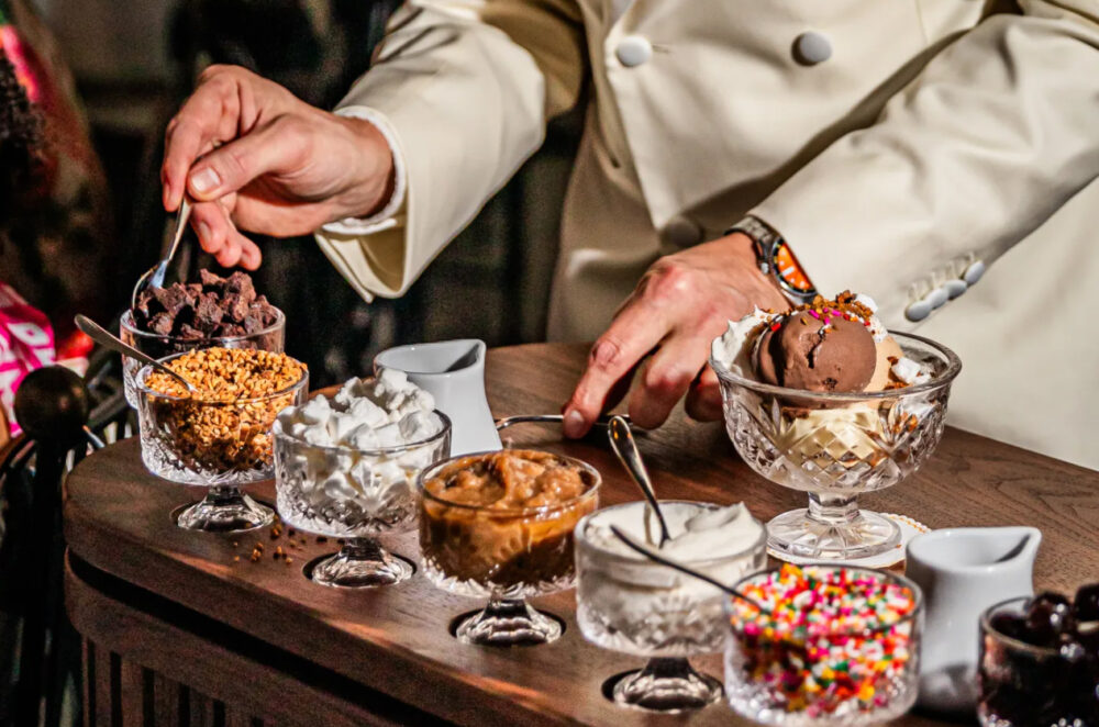 A closeup of a man's hands scooping toppings onto ice cream