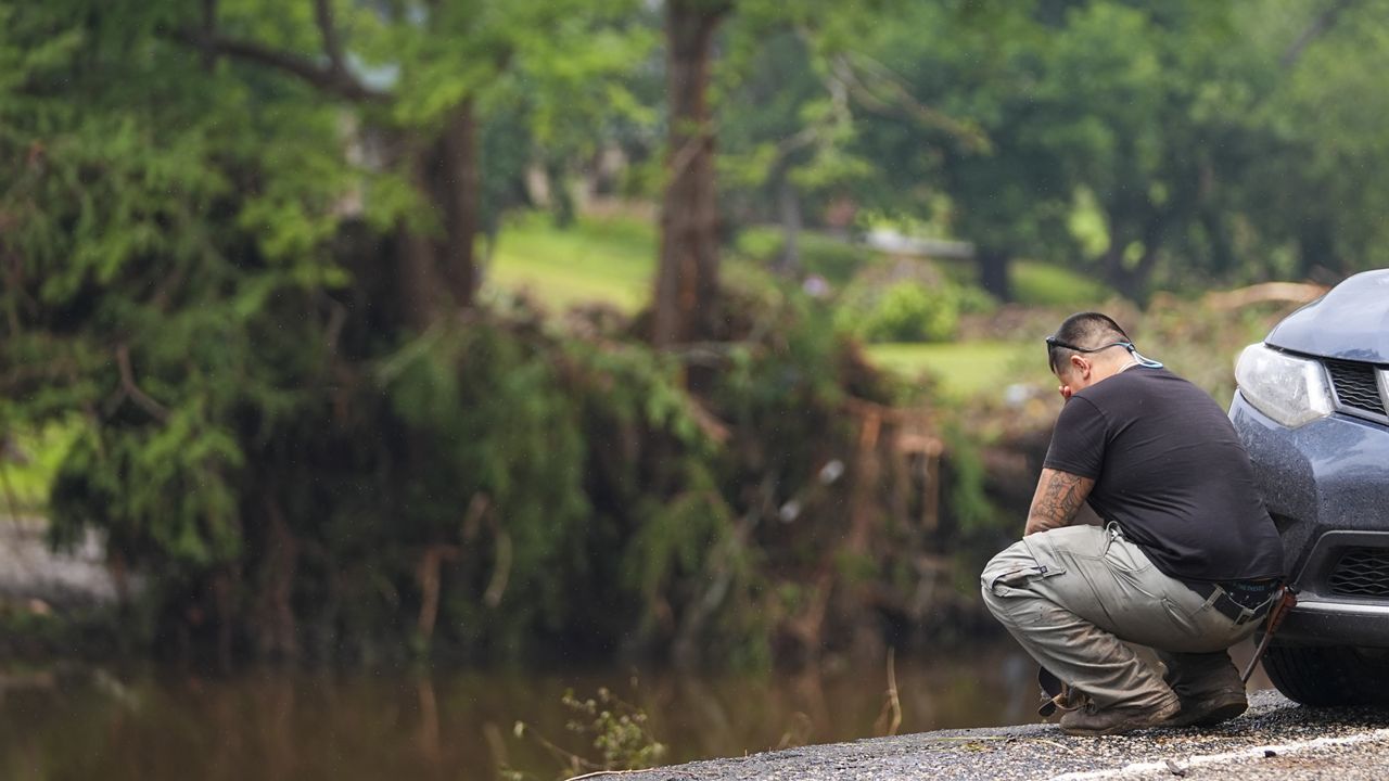 Avi Santos, 23, of San Antonio, Texas, reacts while stopping on the road alongside at Camp Mystic along the banks of the Guadalupe River after a flash flood swept through the area Sunday, July 6, 2025, in Hunt, Texas. (AP Photo/Julio Cortez)