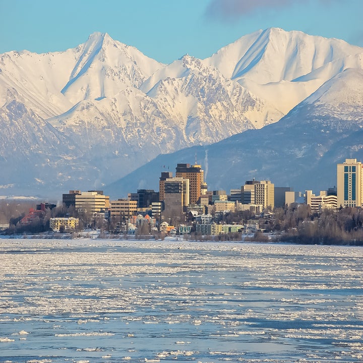 City skyline with snowy mountains in the background and a partially frozen body of water in the foreground