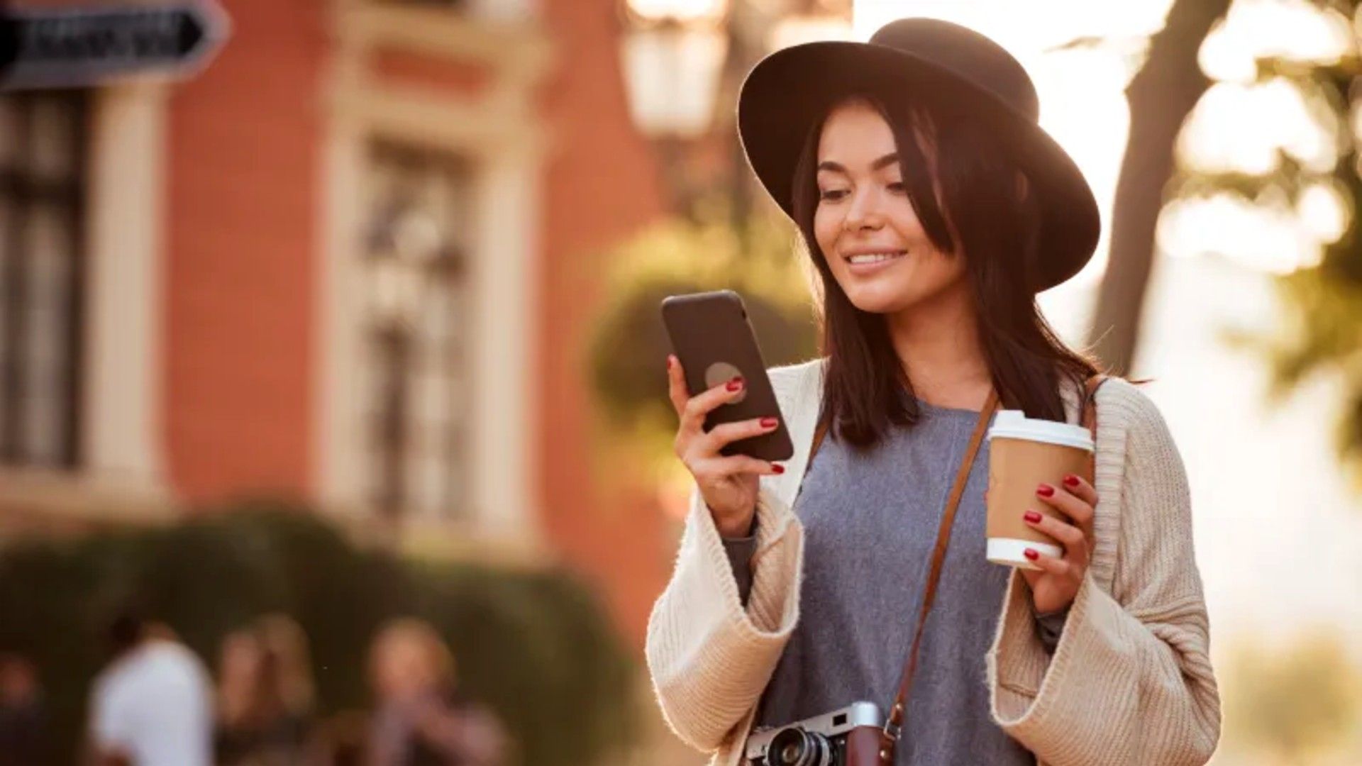 A woman looking at her phone while holding a cup of coffee.
