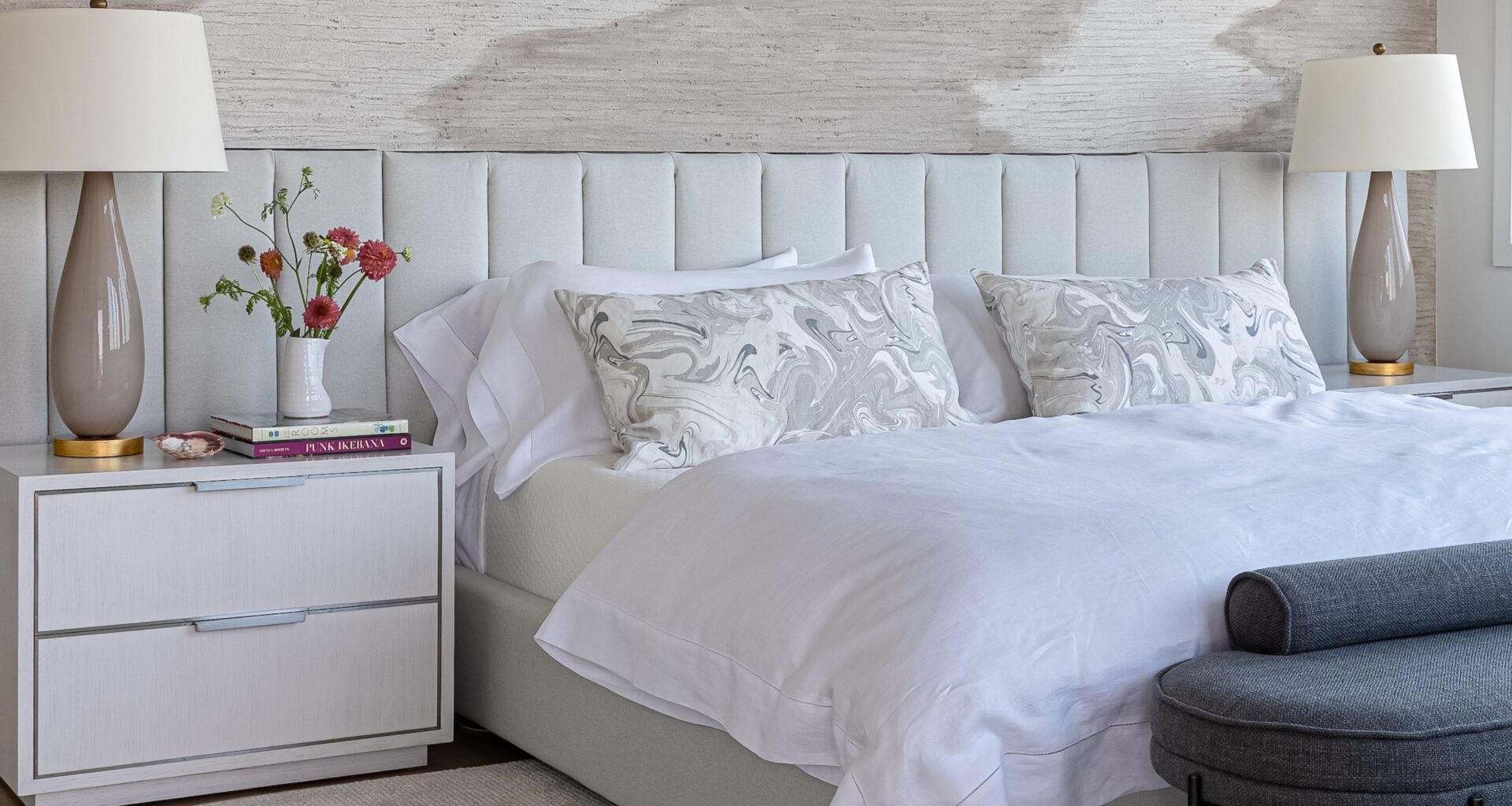 Light, airy bedroom featuring an oversized channel tufted headboard flanked by two nightstands with glossy-based table lamps.