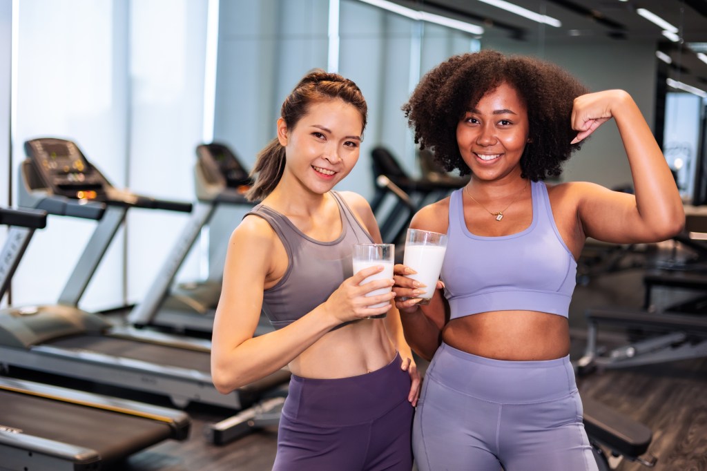 Two women in athletic wear holding protein shakes after a workout.