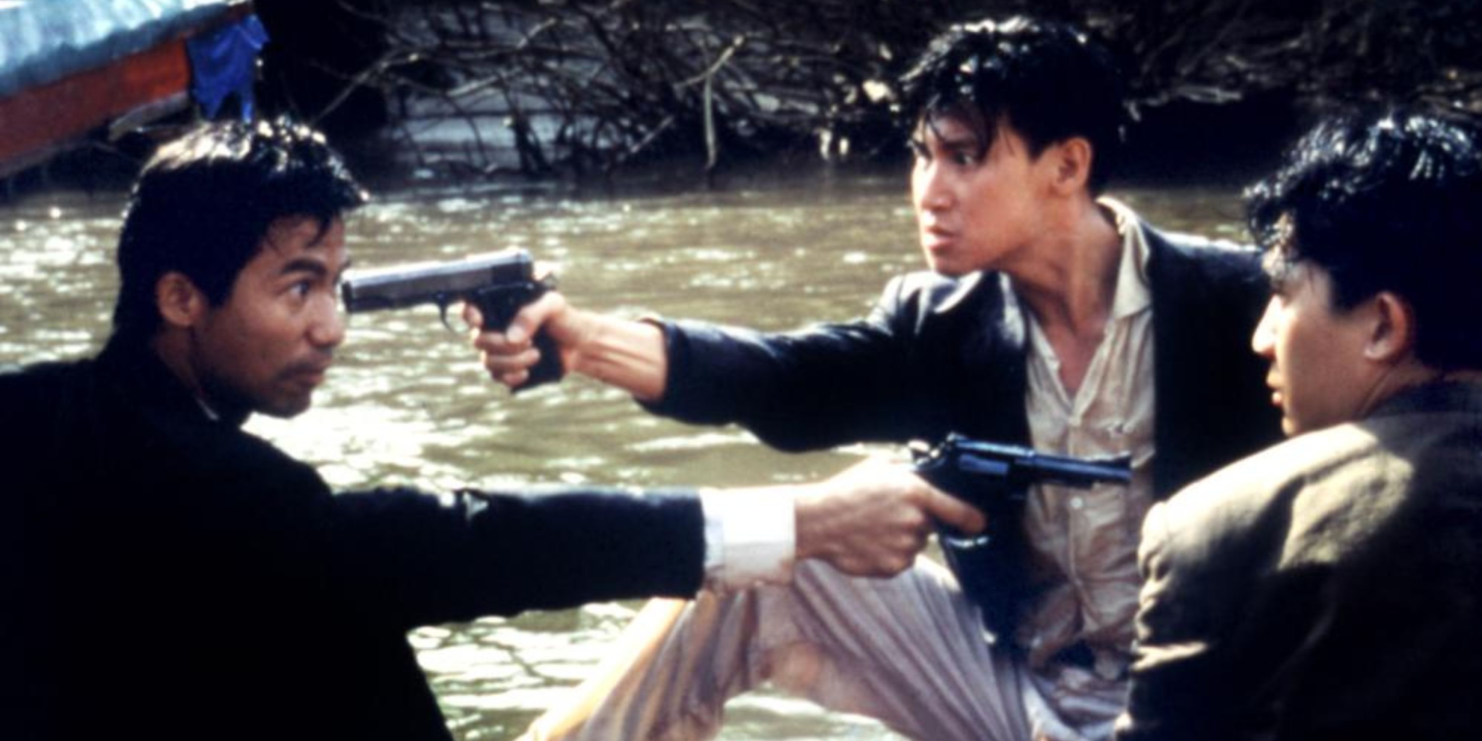 Three men by a river pointing guns at one another in Bullet in the Head - 1990