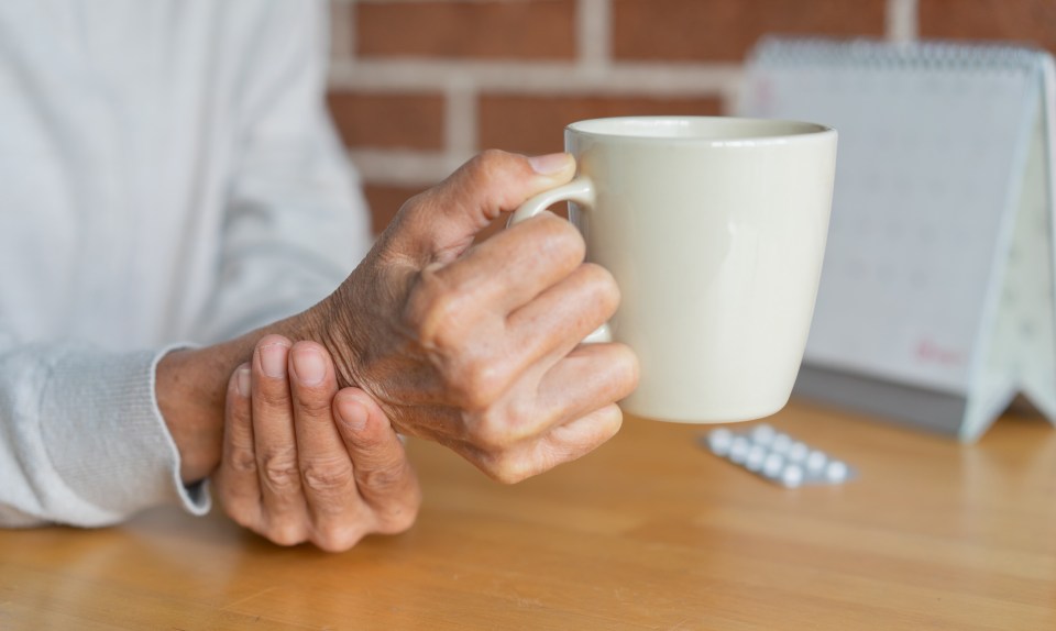Close-up of a senior woman's hand holding a mug, showing symptoms of Parkinson's disease.