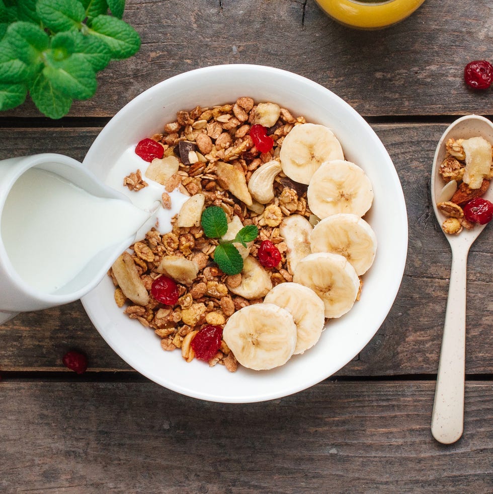 close up of woman pouring milk into bowl with granola
