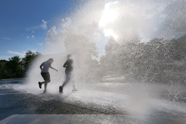 Young people cool off in the spray of an open...