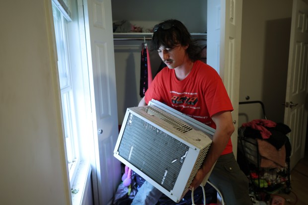 Desmond Quinn hoists an air conditioner to a window ledge at a residence in the Humboldt Park neighborhood on July 11, 2024. Quinn and Sam Diamonte, of the All-Chicago Tenant Alliance program called People's Cooling Army, lend, deliver and install window air conditioners for tenants without adequate cooling in their apartments. (John J. Kim/Chicago Tribune)