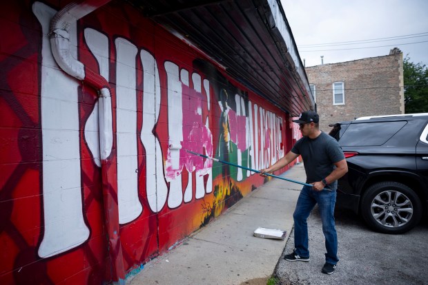 Owner Juan Ocampo paints over graffiti of swastikas on a "Free Palestine" mural by artist Milton Coronado on July 20, 2025, after an overnight vandal tagged their grocery store, La Fruteria, for the second night in a row in the 2700 block of West Cermak Avenue in the Little Village neighborhood of Chicago. (Brian Cassella/Chicago Tribune)