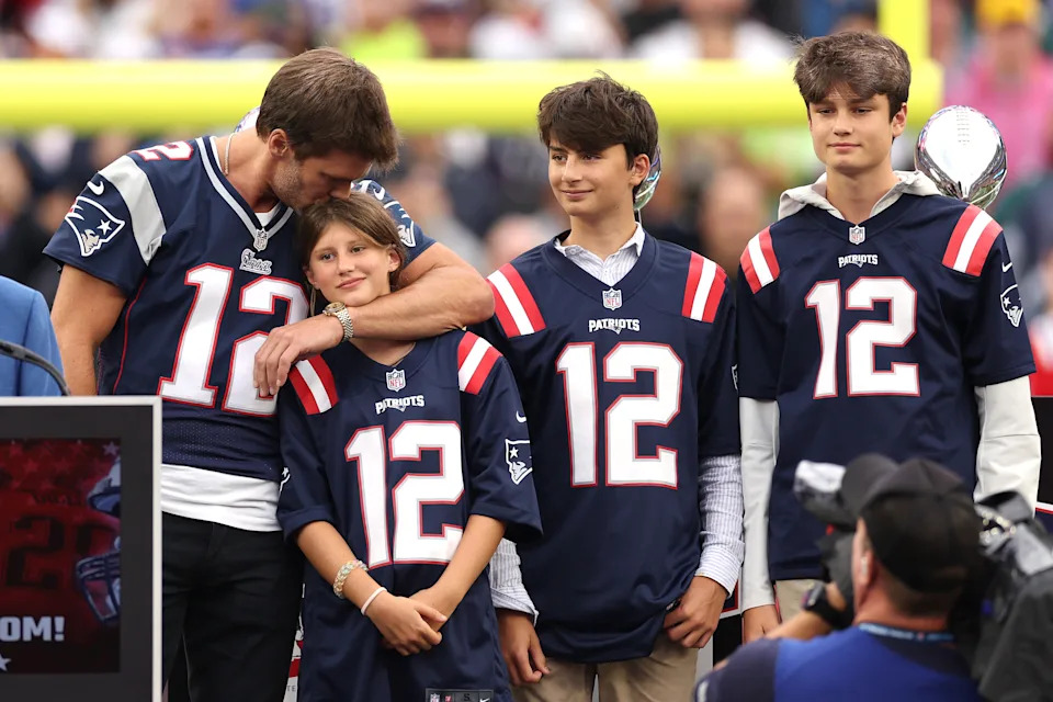 A football player in a jersey embraces a young girl, surrounded by three boys in matching jerseys, on a sports field