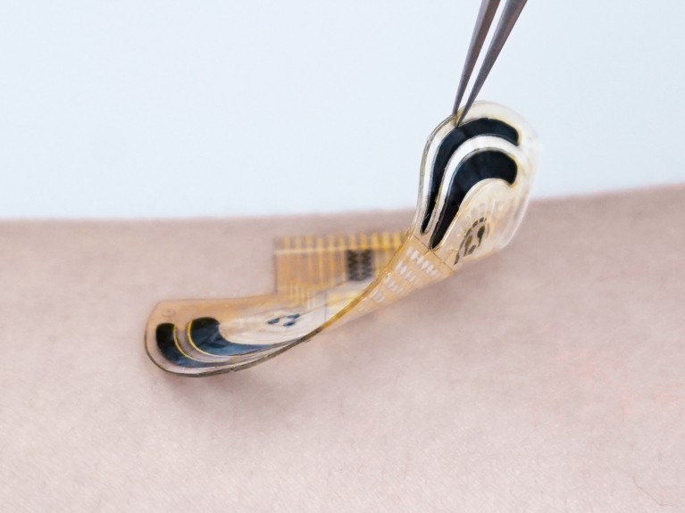 A close-up of tweezers lifting a wafer-thin stress sensor from someone’s skin.