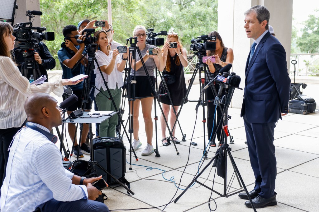 A man in a suit speaks to reporters.
