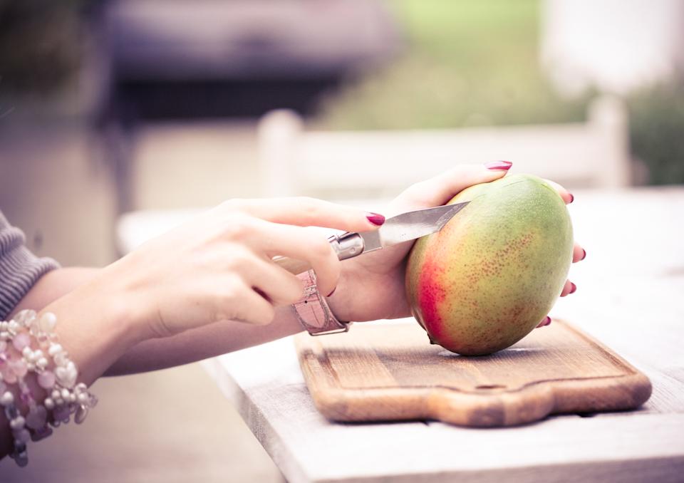 Person cutting mango fruit on wooden board.