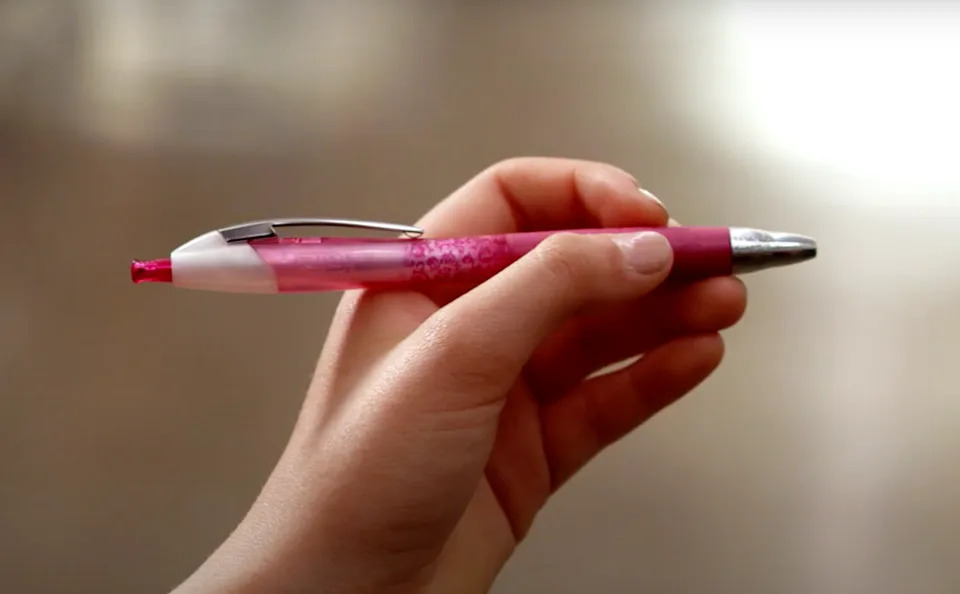 A hand holds a pink retractable pen, poised for use