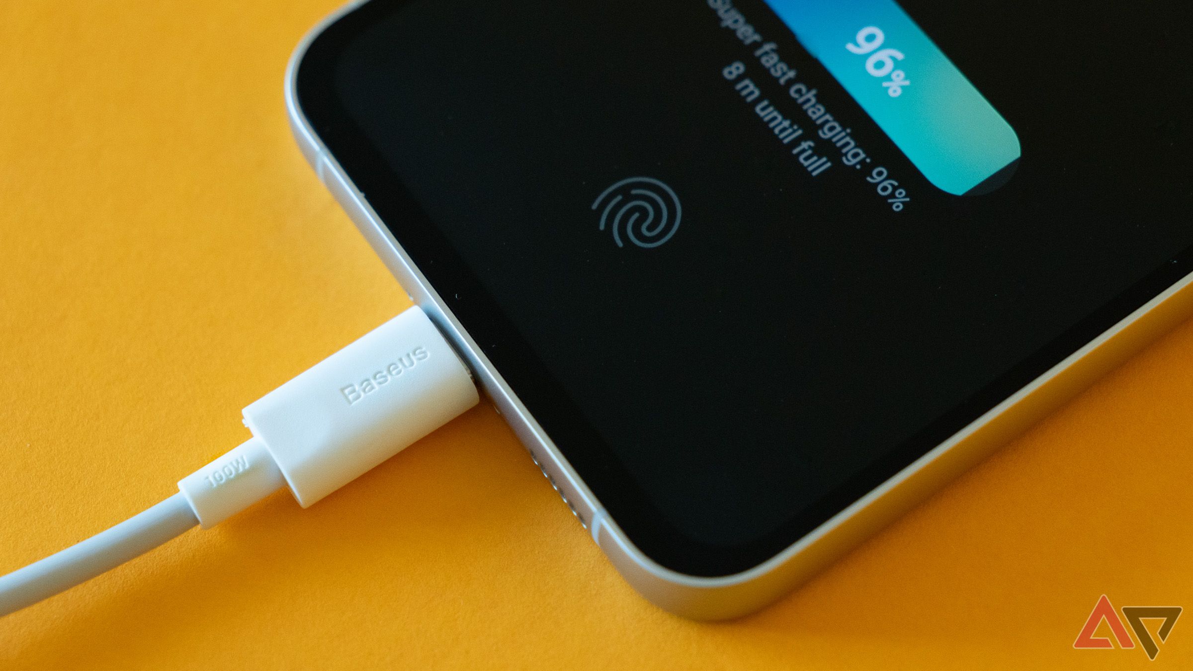 a closeup of a phone charging via cable on yellow surface