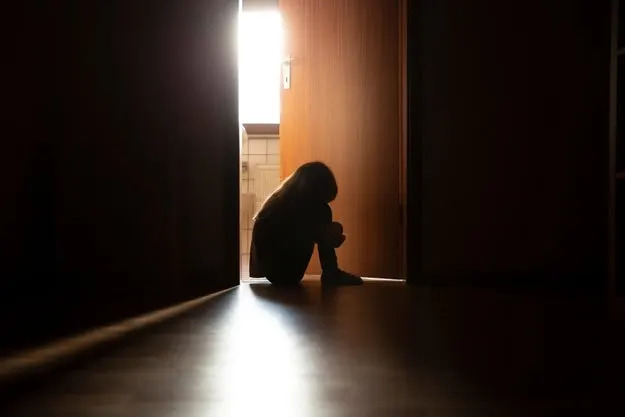 Silhouette of a person sitting on a floor near an open door, light streaming in from behind