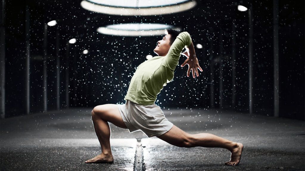 A man doing a yoga pose reminiscent of a warrior pose with an arm extension towards the back, his elbows bent