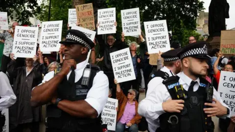 PA Media Police standing in front of protesters holding placards in support of Palestine Action
