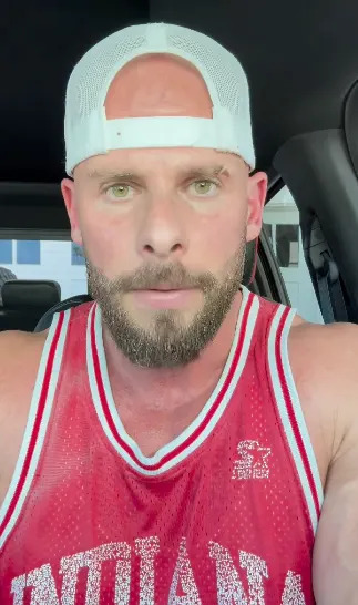 Man in a basketball jersey and white cap sitting in a car, looking at the camera