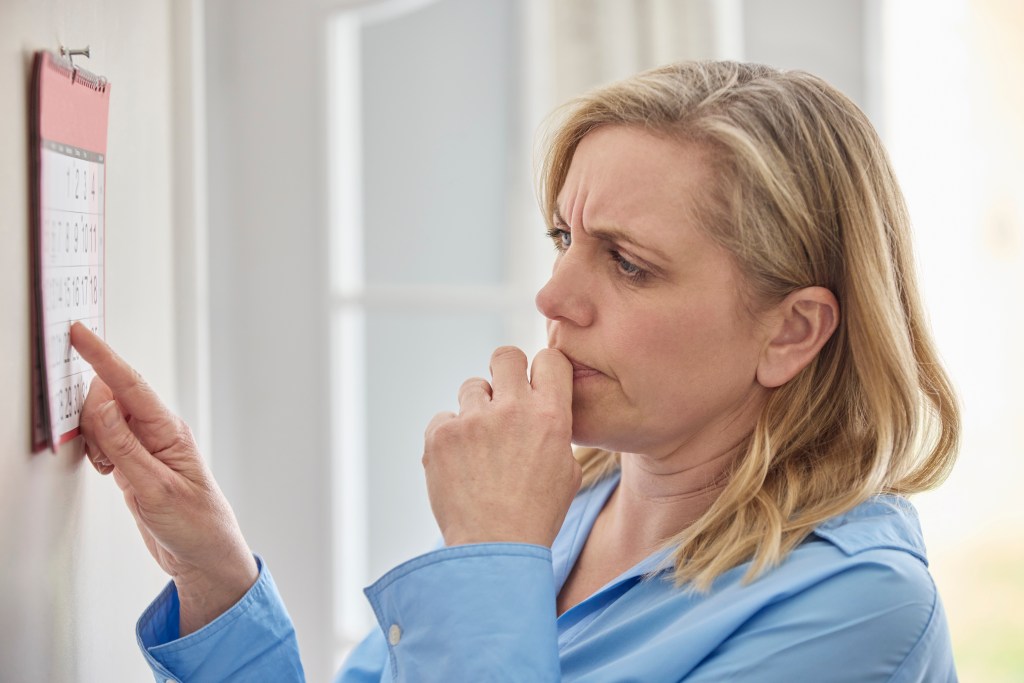 A menopausal woman looks at a calendar, appearing forgetful.