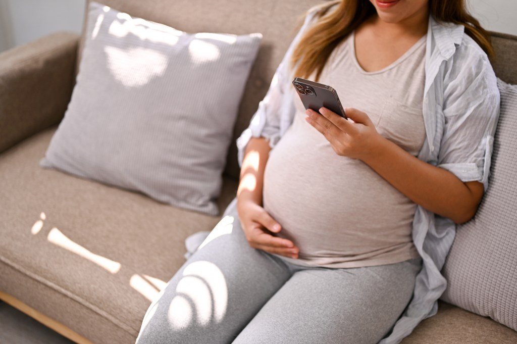 Pregnant woman using phone on sofa.