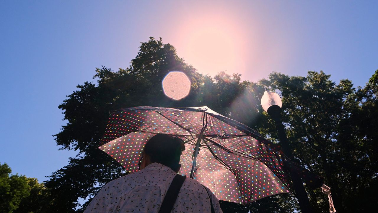 With temperatures hovering near 100 degrees, a woman protects herself from the sun while walking through Boston Common, Tuesday, June 24, 2025, in Boston. (AP Photo/Charles Krupa)