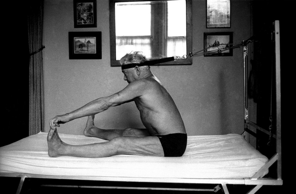 Black and white photo of Joe Pilates demonstrating a Pilates exercise on his "Bednasium."