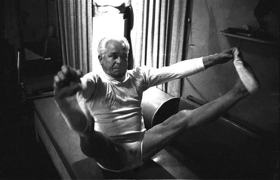 Black and white photo of Joe Pilates demonstrating a Pilates exercise.
