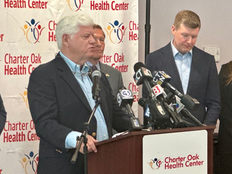 Man in dark blue suit speaks into microphones