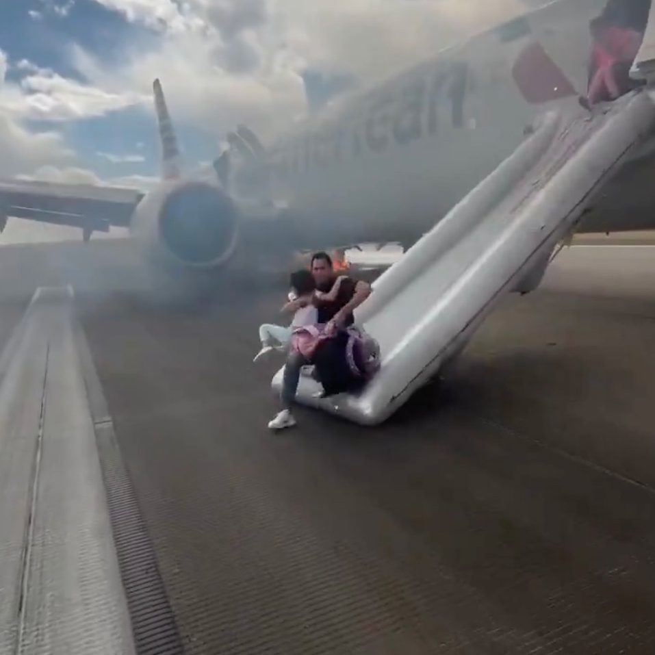 Passenger and child evacuating American Airlines plane via emergency slide.