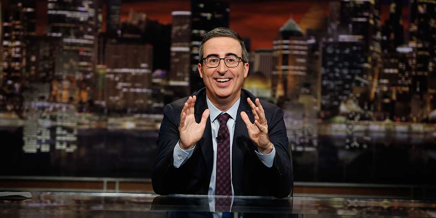 John Oliver with his hands out talking behind the desk in Last Week Tonight with John Oliver.