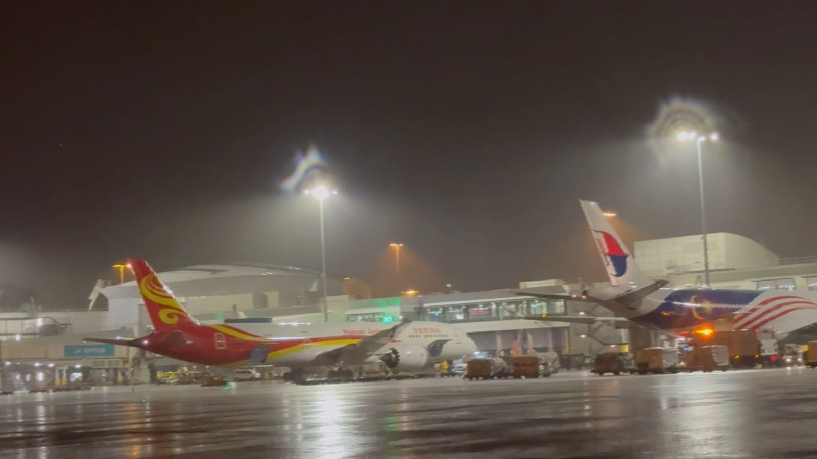 Planes at Sydney Airport under flodolights as rain falls