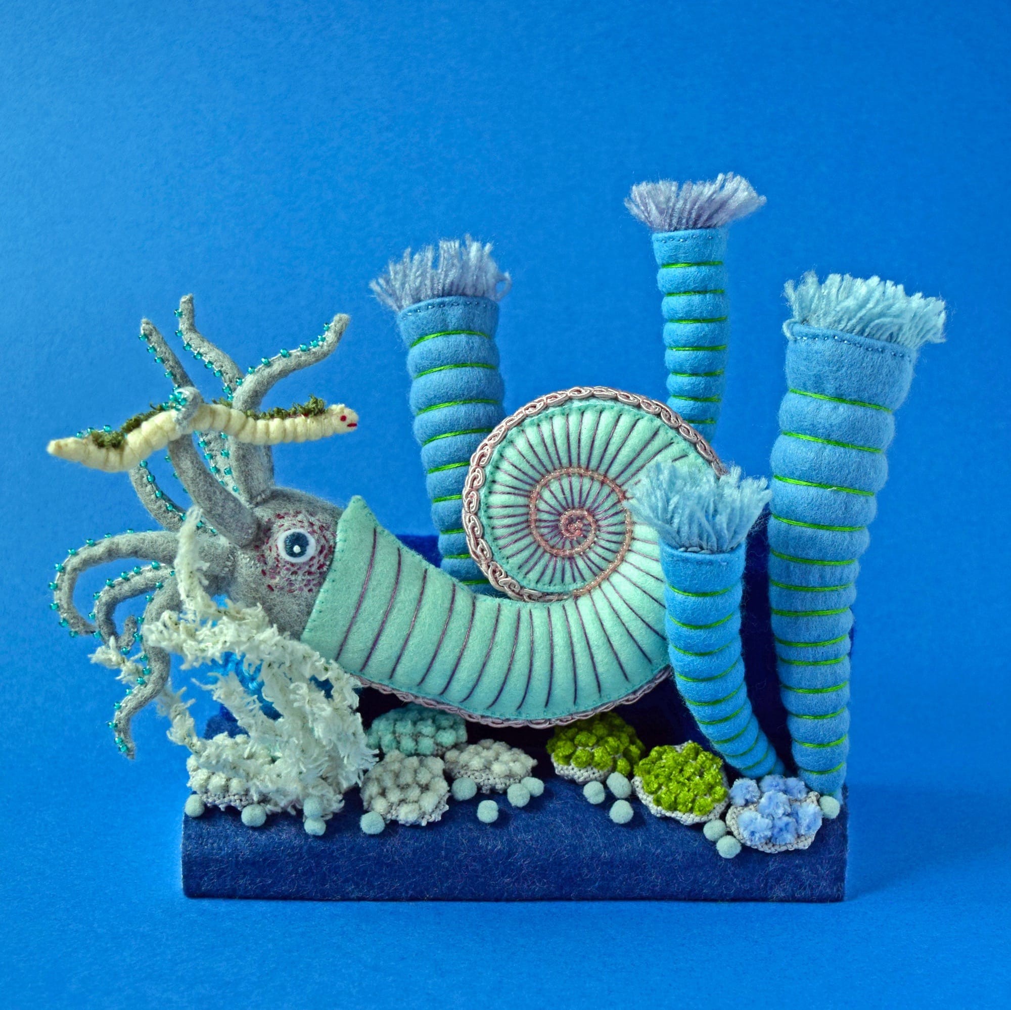 a felted diorama of a blue-green ammonite creature amid coral-like structures