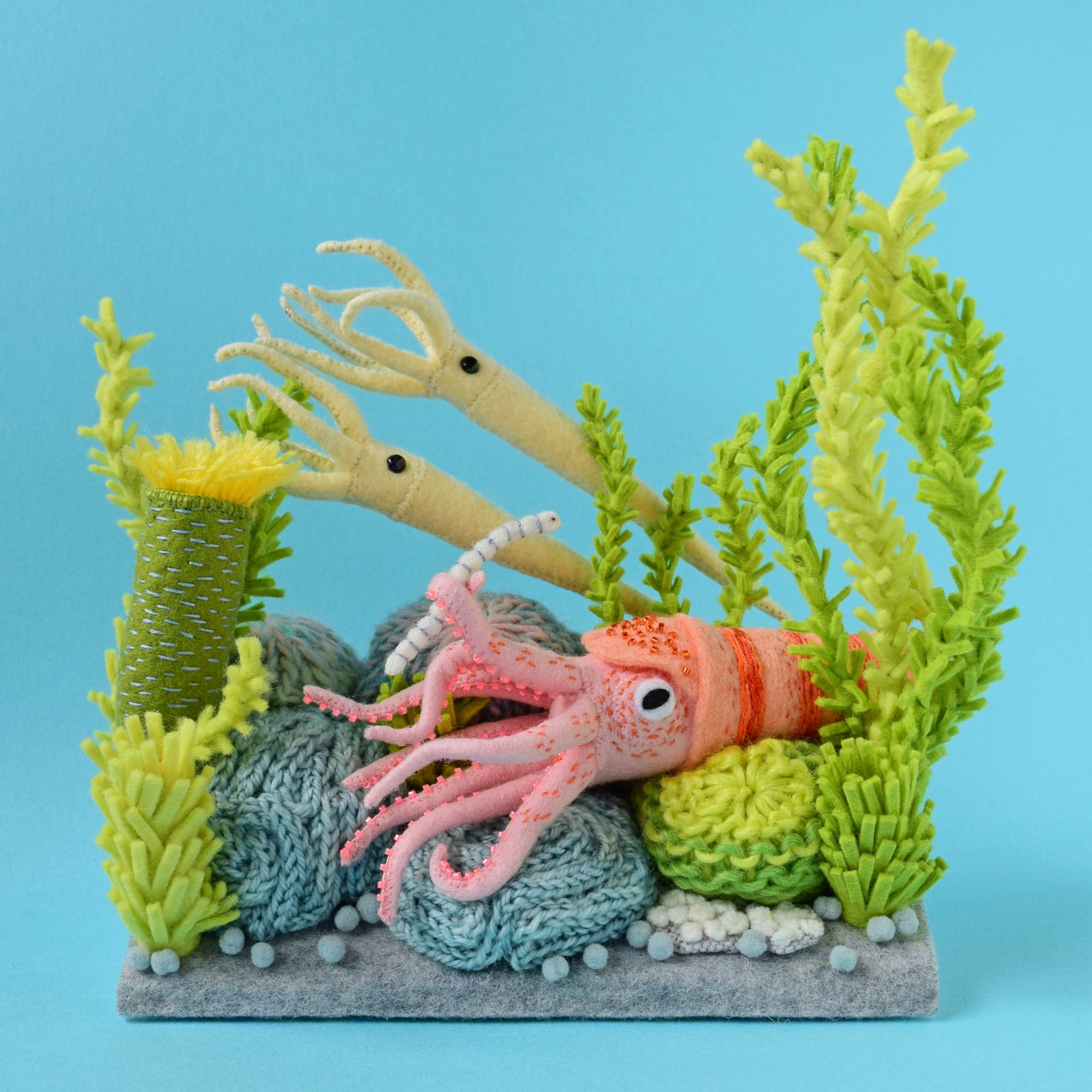 a felted diorama of little pink squid amid seaweed