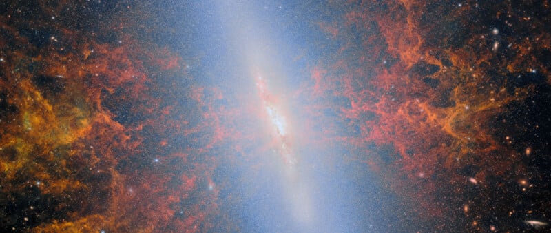 A vibrant, detailed image of a galaxy with a bright white core and swirling red, orange, and yellow clouds of gas and dust, surrounded by a field of stars in deep space.